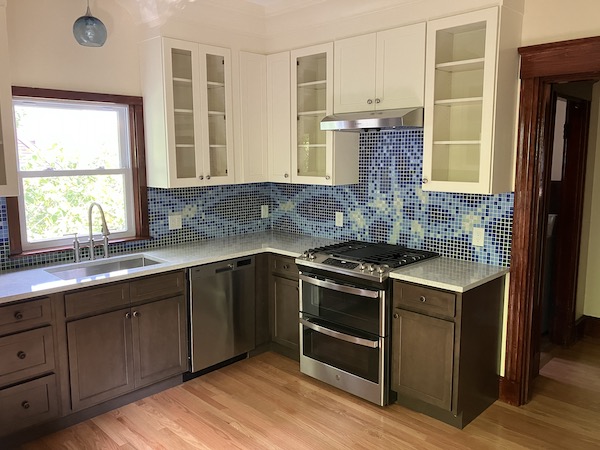 Right-hand view of a kitchen with new appliances, hardwood floor, and custom blue-and-green tile backsplash.