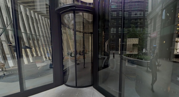 A glass revolving door leading into a boring modern glass building lobby. The number 70 is visible next to the door.