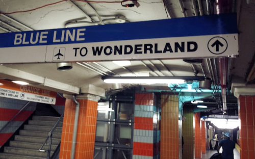 A Boston subway stop. A blue sign reads "Blue Line to Wonderland". In the background, an orange sign says "Orange Line".