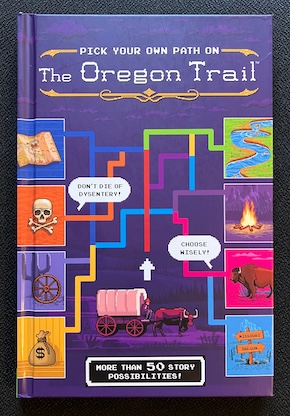 The front cover of "Pick Your Own Path on The Oregon Trail". Branching colored paths connecting panels depicting a river, a map, a campfire, and other thmeatic images. Blurbs say "Don't die of dysentery!" "Choose wisely!" "More than 50 story possibilities!"