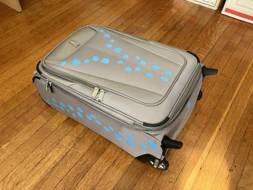 A grey suitcase painted with lines of bright sky-blue spots.