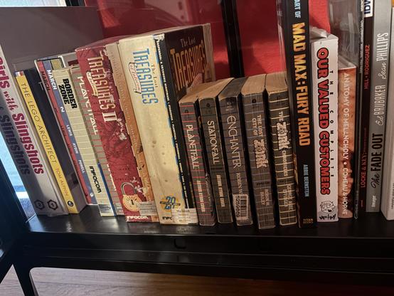 A bookshelf showing 5 of the 6 Infocom tie-in novels next to the Lost Treasures boxed sets and boxed copies of Planetfall and Border Zone