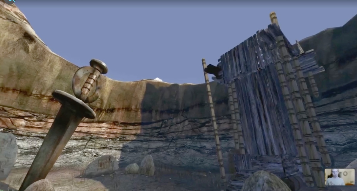 The inside of a steep-sided crater. A large Riven dagger is embedded in the ground. A wooden framework stands to one side by the crater wall. Harley is presenting from a thumbnail in one corner
